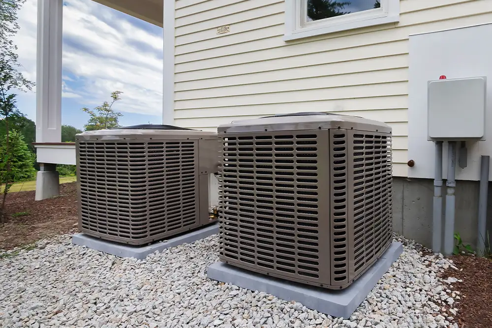 Outdoor condenser units on a gravel pad beside a house